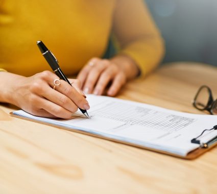 Closeup shot of an unrecognizable woman filling in paperwork on a clipboard at a table